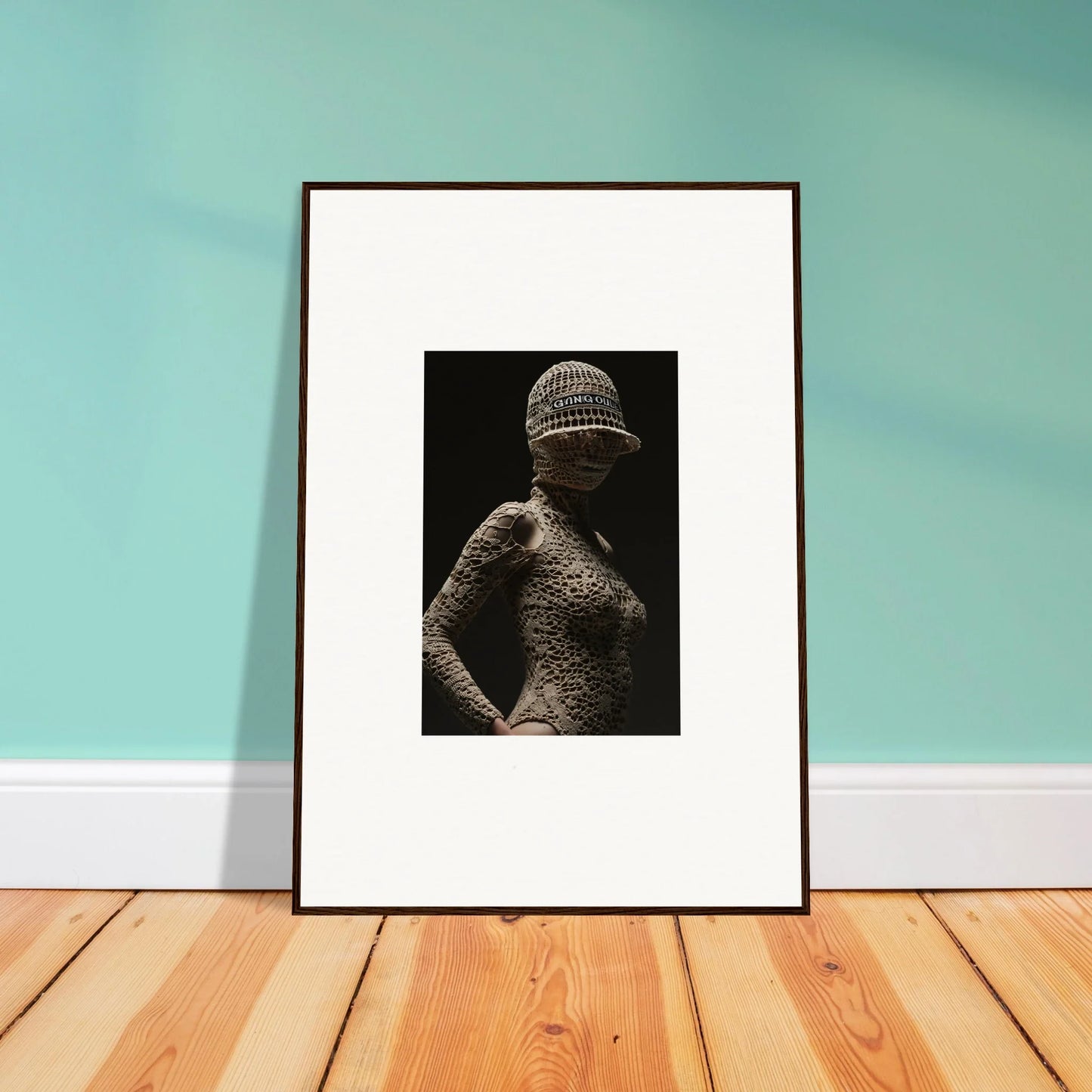 Framed black and white photograph of a figure wearing a textured bodysuit and hat.