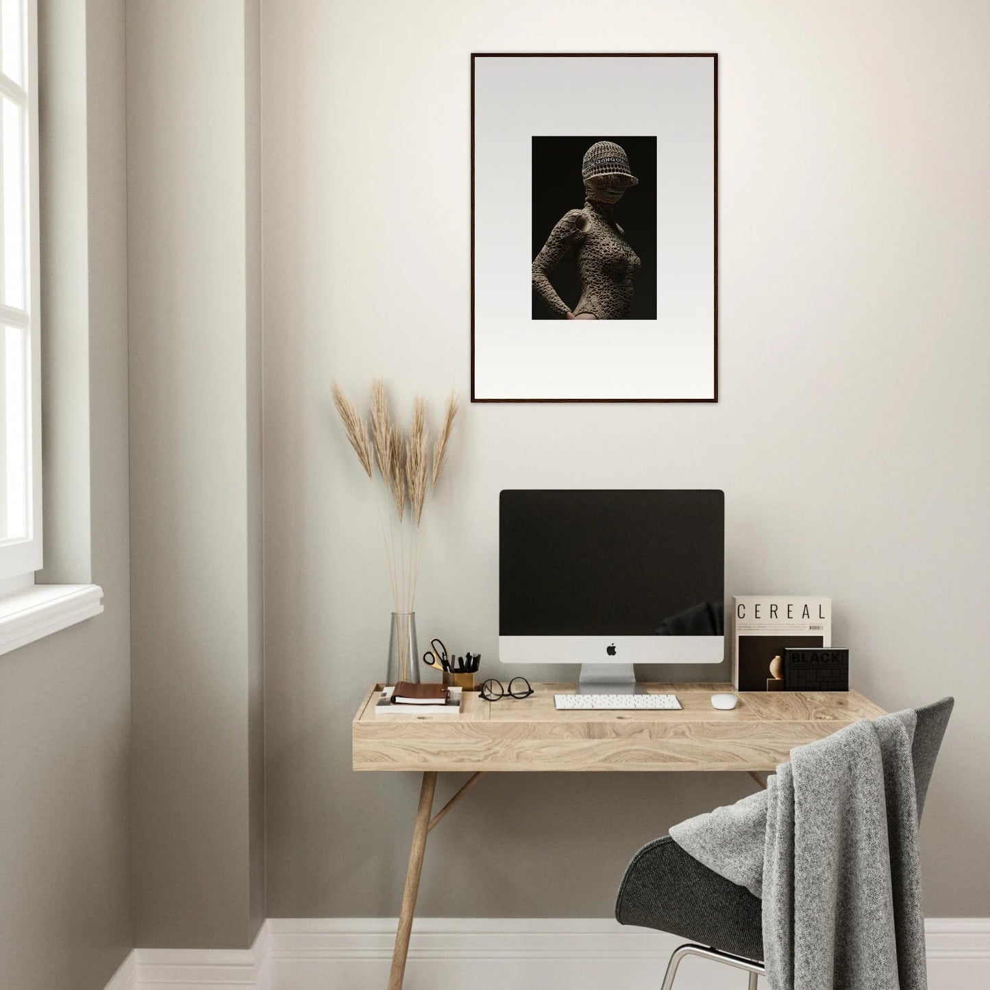 Minimalist home office workspace with a wooden desk, computer, and framed artwork.